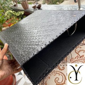 May include: A black binder featuring a textured, embossed geometric pattern on the front cover. The binder is constructed with stitched edges and includes a silver-toned metal ring mechanism visible on the interior side for securing documents.