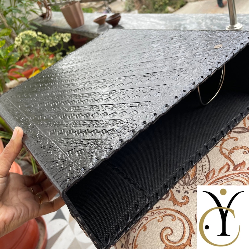 May include: A black binder featuring a textured, embossed geometric pattern on the front cover. The binder is constructed with stitched edges and includes a silver-toned metal ring mechanism visible on the interior side for securing documents.