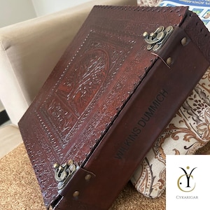 May include: A dark brown leather box featuring an embossed tree design on the lid and two antique brass-coloured metal latches. The side of the box is engraved with the text WILKINS DUMMICH in a dark, capitalised, sans-serif font.