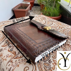 May include: A brown leather journal with a decorative embossed design and a brass lock. The journal measures 8 inches by 6 inches and contains 200 pages. The cover has a flap closure.