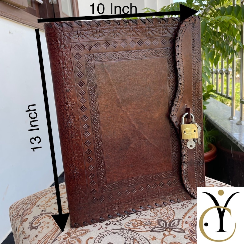 May include: A brown leather journal with a decorative floral and geometric embossed design. The journal is 13 inches tall and 10 inches wide, secured with a leather strap and a gold-colored padlock. The journal is open on a patterned surface.