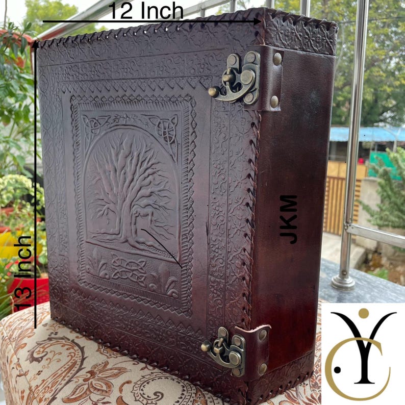 May include: A dark brown leather box featuring an embossed tree design on the front, secured with two antique brass-coloured metal latches. The box measures 12 inches in width and 13 inches in height, with the letters JKM printed on the side panel.
