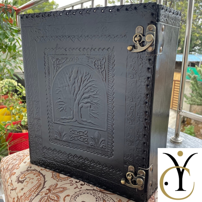 May include: A rectangular black box featuring an embossed tree design on the front panel. The box is constructed with stitched edges and secured by two antique brass-coloured metal latches on the right side. The surface displays intricate patterns.