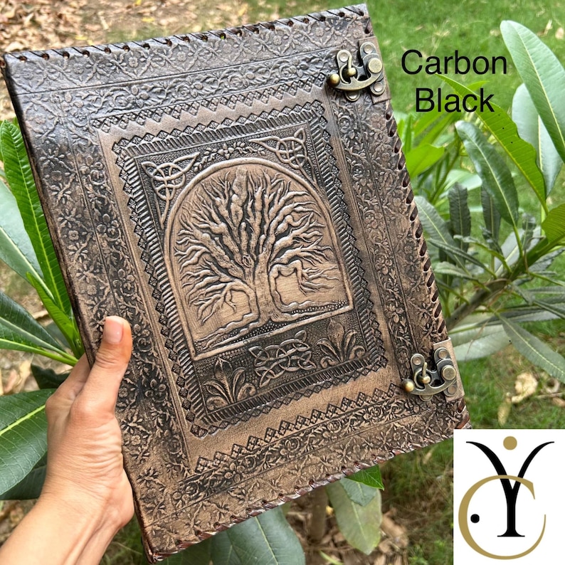 May include: A rectangular carbon black leather journal featuring an embossed tree of life design on the front cover, surrounded by intricate floral and geometric borders. The journal is secured with two antique brass-coloured metal swing latches.