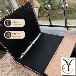 May include: An open ring binder with a tan leather-effect exterior featuring embossed floral patterns and a black interior. The binder includes a 1-inch metal ring mechanism and is designed to hold A4 documents. The edges are stitched with cord.
