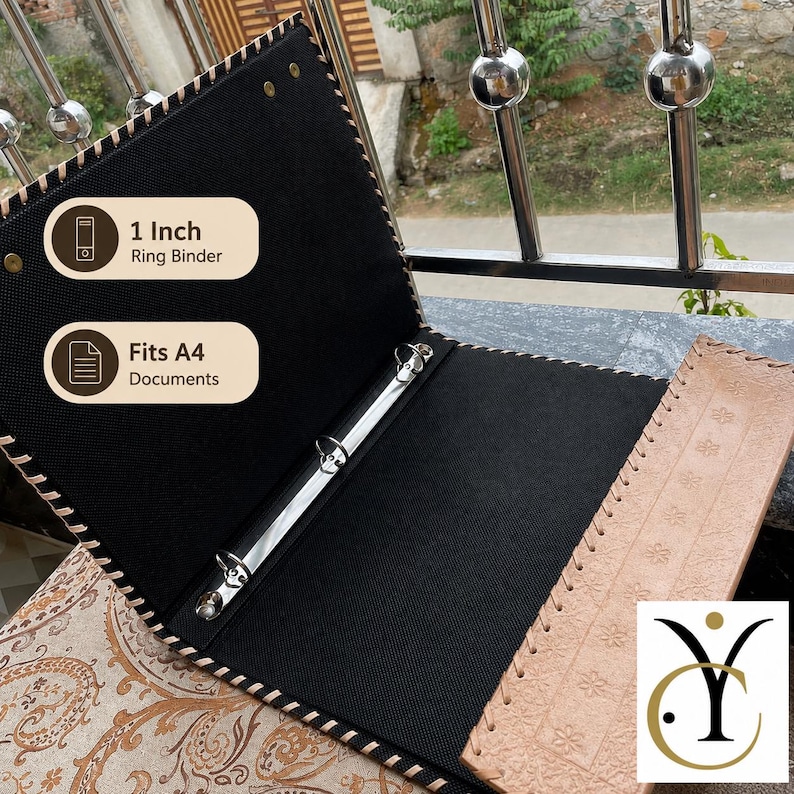 May include: An open ring binder with a tan leather-effect exterior featuring embossed floral patterns and a black interior. The binder includes a 1-inch metal ring mechanism and is designed to hold A4 documents. The edges are stitched with cord.