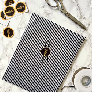 May include: Black and white striped wrapping paper with a gold whisk logo sticker. A pair of silver scissors and a roll of white tape are also in the image.