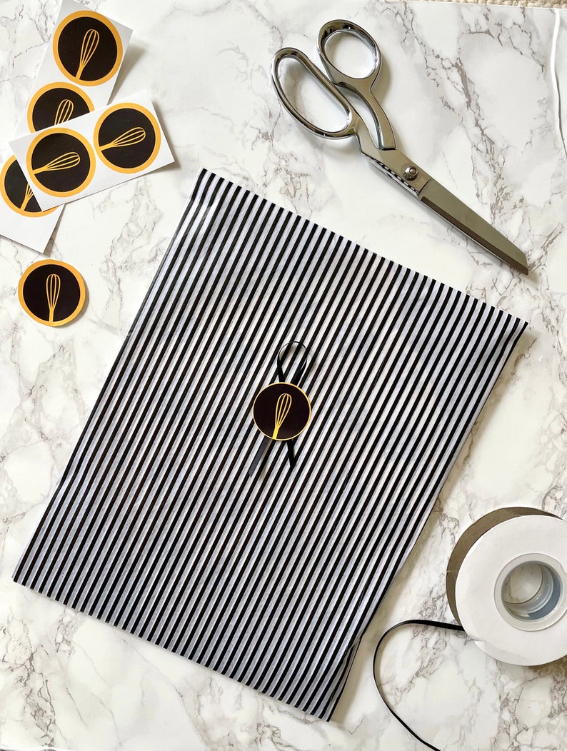 May include: Black and white striped wrapping paper with a gold whisk logo sticker. A pair of silver scissors and a roll of white tape are also in the image.