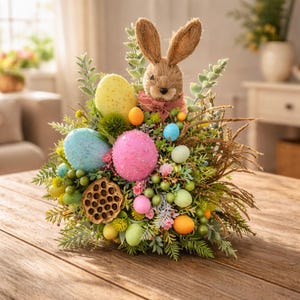 May include: An Easter centrepiece with a brown bunny and long ears, surrounded by speckled eggs in yellow, blue, and pink. The arrangement includes green foliage, small berries, and decorative accents, creating a festive spring display.