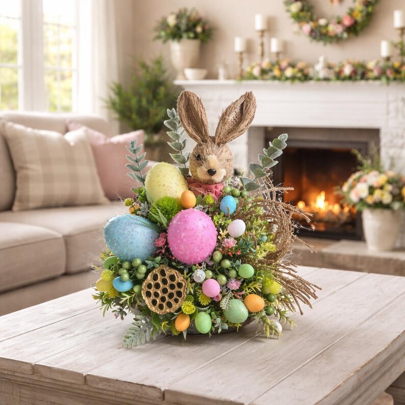 May include: An Easter centrepiece with a brown rabbit figure and long ears, surrounded by speckled eggs in blue, pink, and yellow. The arrangement includes greenery, small flowers, and decorative elements, creating a festive spring display.