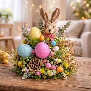 May include: An Easter display with a bunny head and a pink bow, surrounded by pastel-coloured eggs, foliage, and flowers. The eggs are yellow, blue, and pink. The arrangement is on a wooden table, creating a festive spring scene.