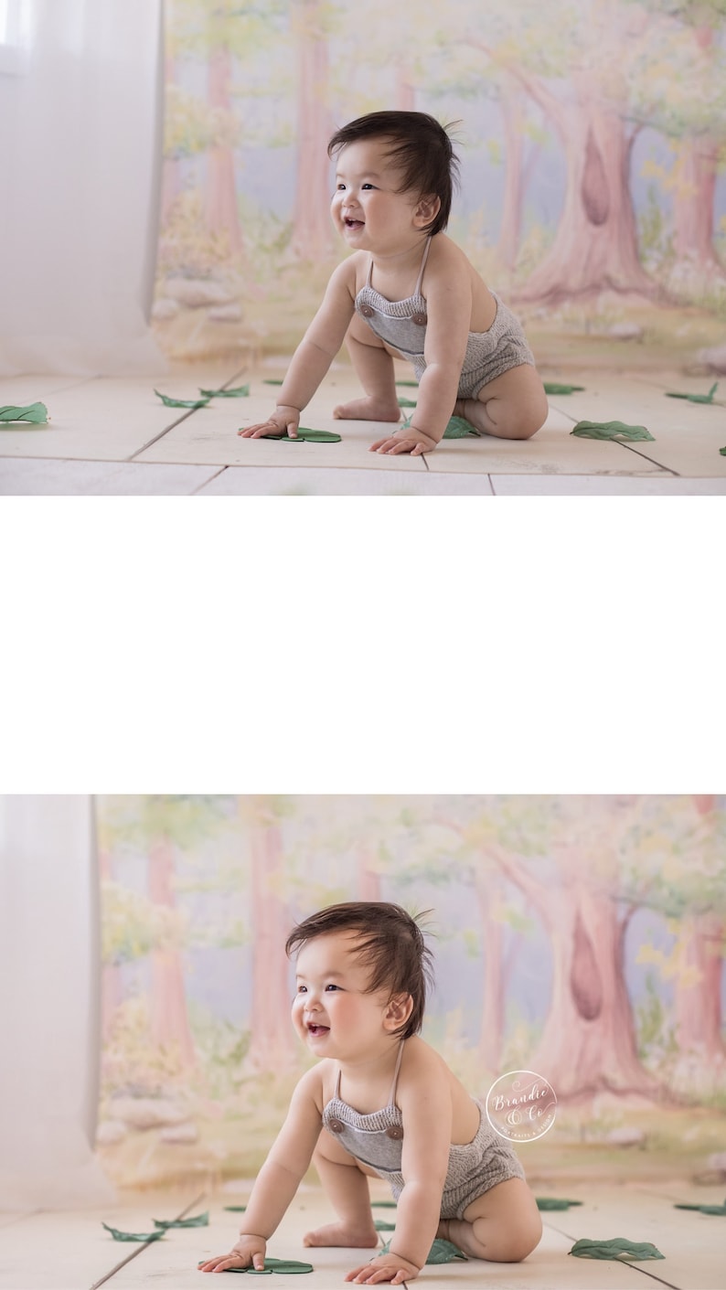 May include: A baby in a gray onesie with brown buttons sits on a white floor with green leaves scattered around. The baby is smiling and looking to the right. The background is a painted mural of a forest with pink, green, and blue colors.