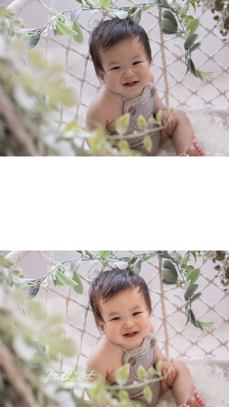 May include: A baby wearing a light brown overall with a white background. The baby is sitting in a white hammock with green leaves hanging from it. The baby is smiling and looking at the camera.
