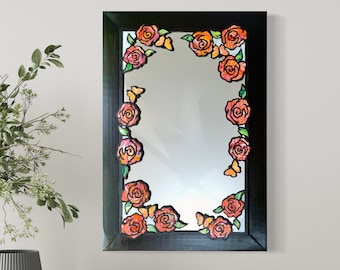 May include: A black framed mirror with a stained glass design featuring orange and red roses and butterflies around the perimeter.