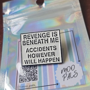 May include: A white enamel pin with the text "REVENGE IS BENEATH ME ACCIDENTS HOWEVER WILL HAPPEN" in black. The pin is on a striped card with a QR code and the "moo pals" logo, inside a holographic bag.
