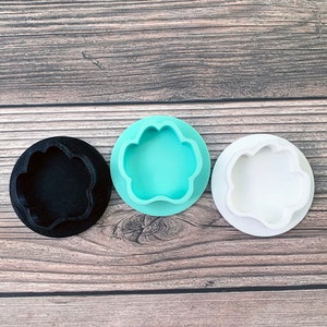Puede incluir: Tres cortadores de galletas con forma de huella de pata, uno negro, uno turquesa y uno blanco.