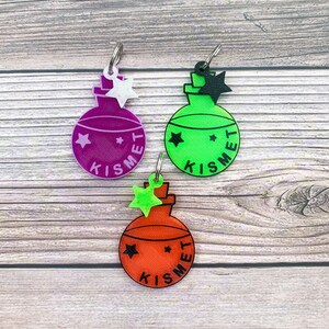 May include: Three colorful glass bottle charms with a star on top and the word "Kismet" written on the side. The charms are purple, green, and orange.