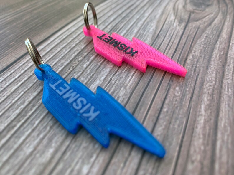 May include: Two lightning bolt shaped keychains, one pink and one blue, with the word "Kismet" printed on each.