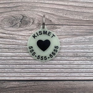 May include: A round, glow-in-the-dark pet ID tag with a black heart and the text "KISMET 555-555-5555".