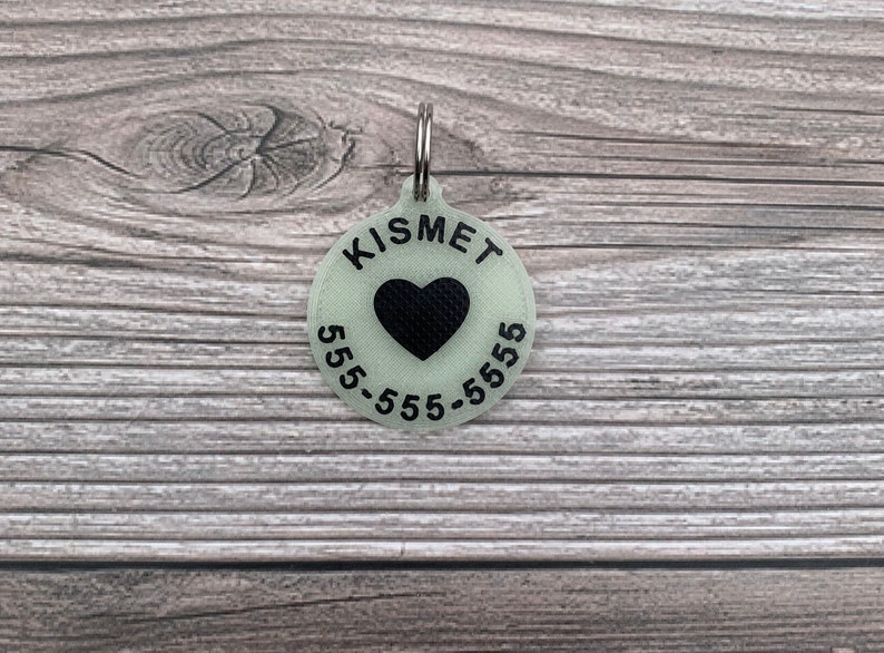 May include: A round, glow-in-the-dark pet ID tag with a black heart and the text "KISMET 555-555-5555".