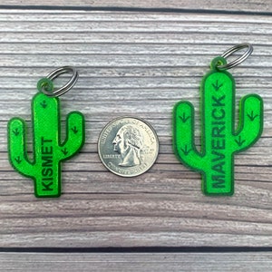 May include: Two green cactus-shaped keychains with silver key rings. The cactus on the left says "Kismet" and the cactus on the right says "Maverick".