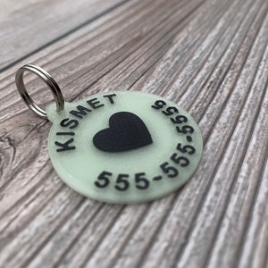 May include: A round, glow-in-the-dark pet tag with a black heart and the text "KISMET 555-555-5555".