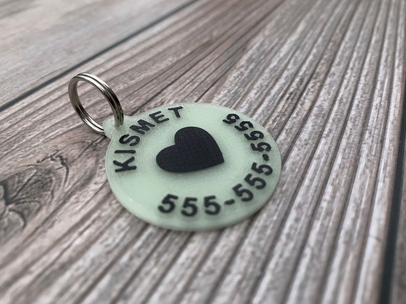May include: A round, glow-in-the-dark pet tag with a black heart and the text "KISMET 555-555-5555".