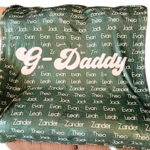 May include: Green fleece blanket with the text "G-Daddy" in pink cursive lettering. The blanket is covered in a repeating pattern of names, including "Leah", "Zander", "Theo", "Jack", and "Evan".