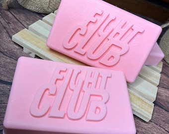 May include: Two pink soap bars with the words "Fight Club" embossed on them. The soap bars are sitting on a wooden surface.