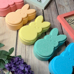 Könnte beinhalten: Fünf pastellfarbene Badebomben in Form von Osterhasen. Die Badebomben sind rosa, orange, gelb, grün und blau.