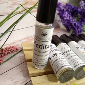 May include: Three small glass bottles with roller balls, each containing a different essential oil blend. The bottles are labelled "Meditate", "Support", and "Headache Relief". Each bottle is handmade in Colorado and contains coconut oil, lavender, and other essential oils. The bottles are sitting on a wooden surface.