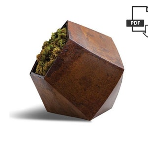 Może przedstawiać: Geometryczny kwietnik w kolorze rdzawego brązu z rośliną mchu w środku. Kwietnik jest wykonany z metalu i ma unikalny, kanciasty design.