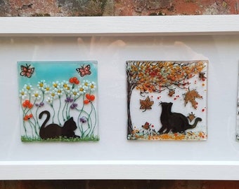 A cat for all seasons. Framed art. Black cat. Fused glass panels. four glass art pictures. White box frame. spring. Summer. Autumn. Winter.