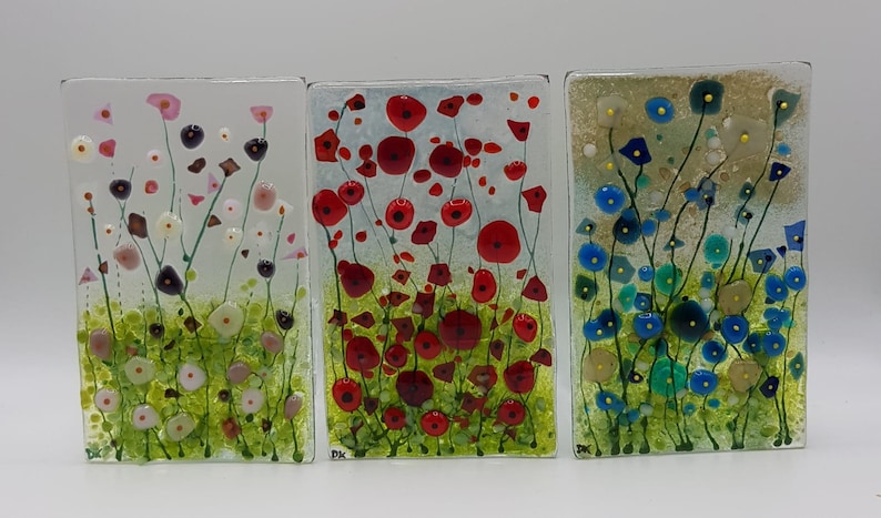 May include: Three rectangular glass panels with a floral design. The first panel features pink and white flowers with green stems. The second panel features red flowers with green stems. The third panel features blue flowers with green stems.