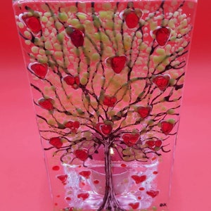 May include: A glass tealight holder featuring a tree with red hearts for leaves. The tree is surrounded by smaller red hearts and a clear glass tealight holder.