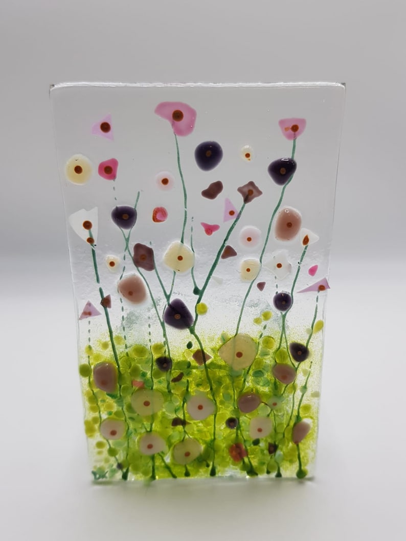 May include: A glass art piece depicting a field of wildflowers. The flowers are pink, white, and purple, with green stems and leaves. The background is a light blue.