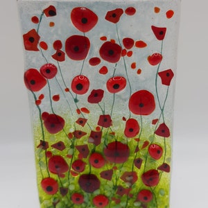 May include: A glass art piece featuring a field of red poppies with green stems and leaves on a white background. The piece is rectangular and has a textured surface.