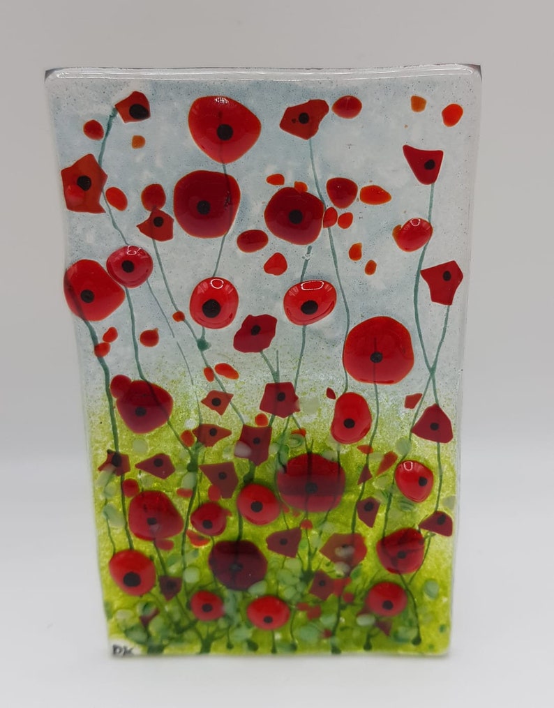 May include: A glass art piece featuring a field of red poppies with green stems and leaves on a white background. The piece is rectangular and has a textured surface.