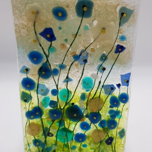 May include: A glass art piece featuring a field of blue, green, and yellow flowers. The flowers are abstract and have a textured look. The background is a light beige color.