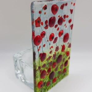 May include: A glass candle holder with a red poppy flower design. The holder is clear glass and has a square shape. The flowers are painted in red, green, and white.