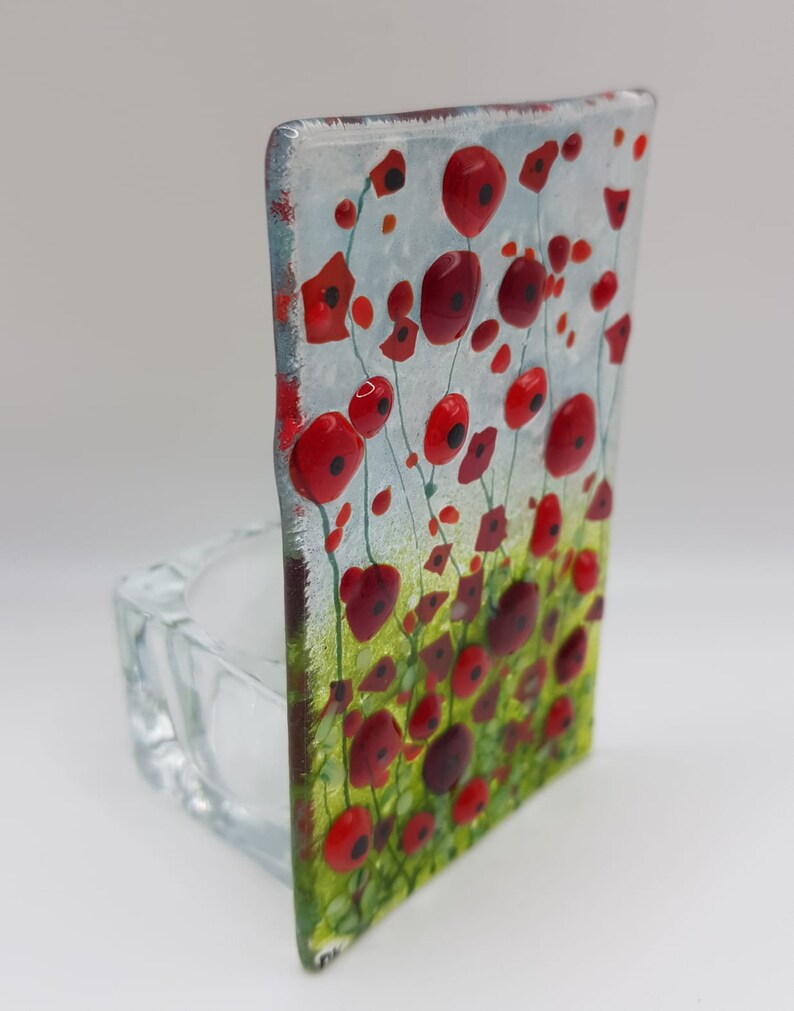 May include: A glass candle holder with a red poppy flower design. The holder is clear glass and has a square shape. The flowers are painted in red, green, and white.