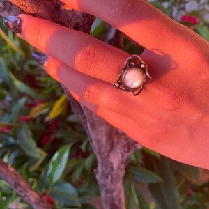 May include: A silver ring with a large, white pearl-like stone set in a delicate, twisted wire design.
