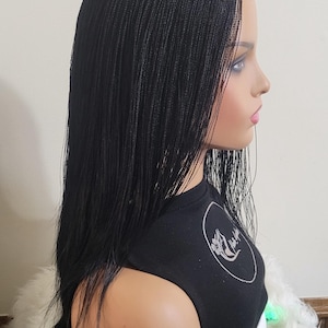 May include: A black braided wig on a mannequin head. The wig is styled with long, straight braids. The mannequin is wearing a black top with a white graphic. The background is a plain white wall.