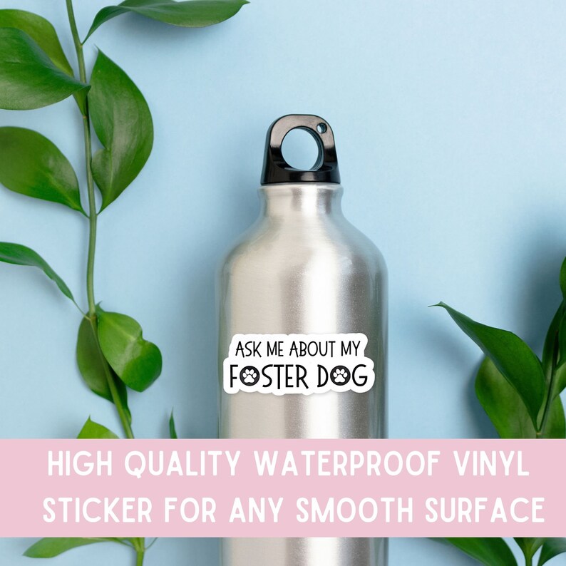 K&ouml;nnte beinhalten: Eine silberne Wasserflasche mit schwarzem Deckel und einem wei&szlig;en Aufkleber mit der Aufschrift "ASK ME ABOUT MY FOSTER DOG" in schwarzer Schrift. Der Aufkleber hat ein Pfotenabdruck-Design. Gr&uuml;ne Bl&auml;tter und ein hellblauer Hintergrund sind sichtbar.