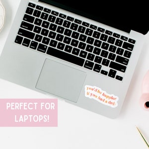 May include: A silver laptop computer with a sticker on the right side of the trackpad. The sticker is white with pink and orange text that reads "you'd be happier if you had a dog."