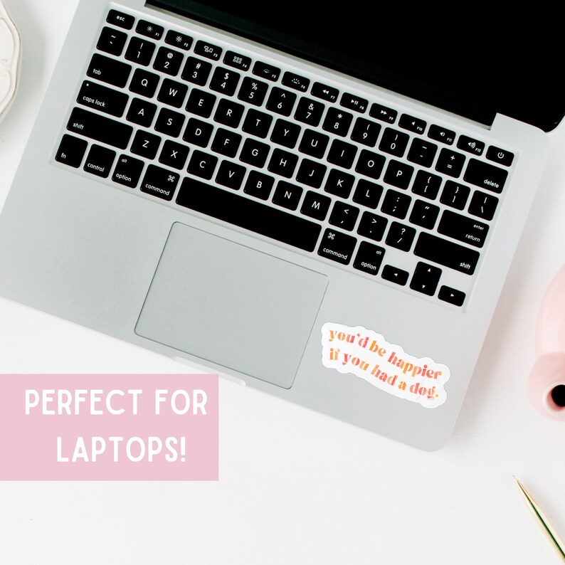 May include: A silver laptop computer with a sticker on the right side of the trackpad. The sticker is white with pink and orange text that reads "you'd be happier if you had a dog."