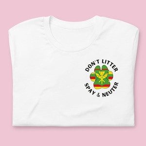 May include: White t-shirt with a black paw print design. The paw print is filled with the colors of the Rastafarian flag: green, yellow, and red. The text around the paw print reads "Don't Litter Spay & Neuter".