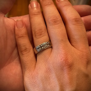 May include: A silver ring with the inscription "Per aspera ad astra" on it.