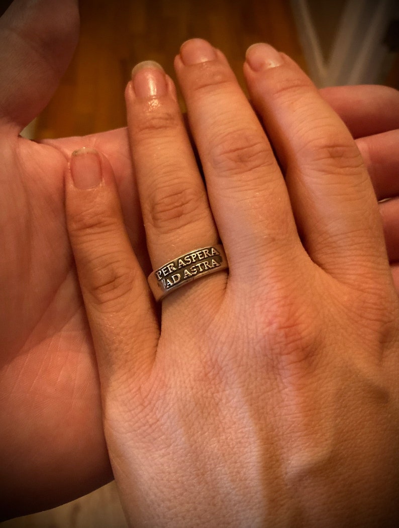 May include: A silver ring with the inscription "Per aspera ad astra" on it.