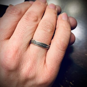 May include: A silver ring with the inscription "Per Aspera Ad Astra" on a person's finger.